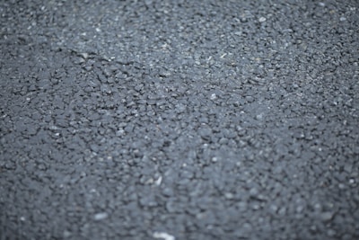 A close-up view of a rough asphalt surface, displaying a textured pattern made up of small, irregularly shaped stones and gravel.