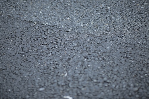 A close-up view of a rough asphalt surface, displaying a textured pattern made up of small, irregularly shaped stones and gravel.