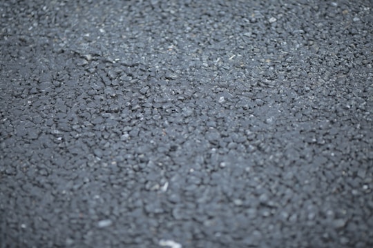 A close-up view of a rough asphalt surface, displaying a textured pattern made up of small, irregularly shaped stones and gravel.