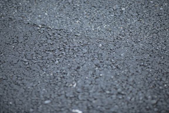 A close-up view of a rough asphalt surface, displaying a textured pattern made up of small, irregularly shaped stones and gravel.