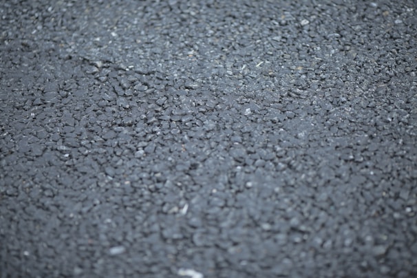A close-up view of a rough asphalt surface, displaying a textured pattern made up of small, irregularly shaped stones and gravel.