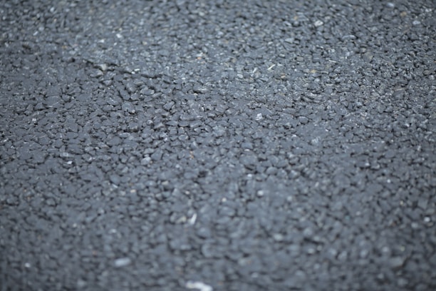 A close-up view of a rough asphalt surface, displaying a textured pattern made up of small, irregularly shaped stones and gravel.
