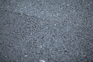 A close-up view of a rough asphalt surface, displaying a textured pattern made up of small, irregularly shaped stones and gravel.