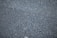 A close-up view of a rough asphalt surface, displaying a textured pattern made up of small, irregularly shaped stones and gravel.