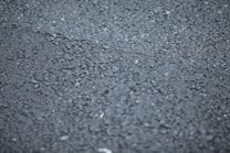 A close-up view of a rough asphalt surface, displaying a textured pattern made up of small, irregularly shaped stones and gravel.