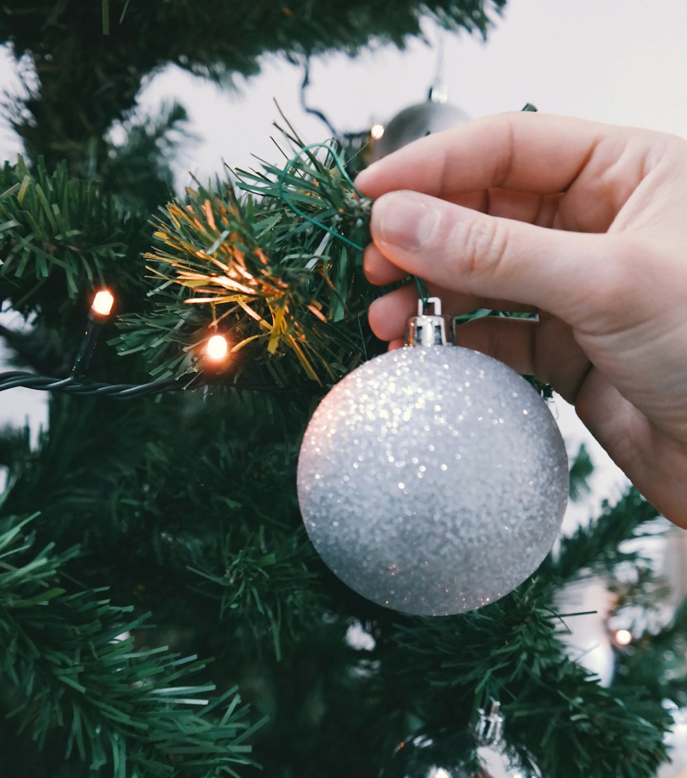 A person hanging a silver ornament to an XMAS tree.