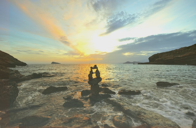 Sunset over a calm beach with gentle waves and scattered rocks.