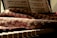 A sheet of music rests on a stand above a piano keyboard. A textured fabric with intricate patterns covers parts of the piano, with sunlight casting warm tones and soft shadows over the scene.