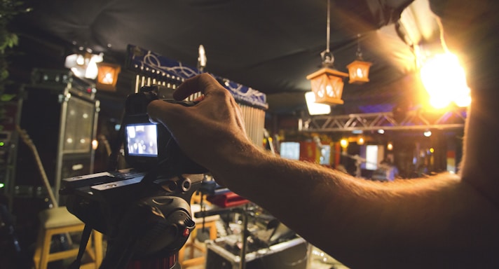 A warm-toned photo showing a creative professional adjusting a camera on set, surrounded by lighting equipment.