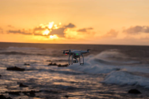 A sleek drone hovering over a scenic landscape at sunset.