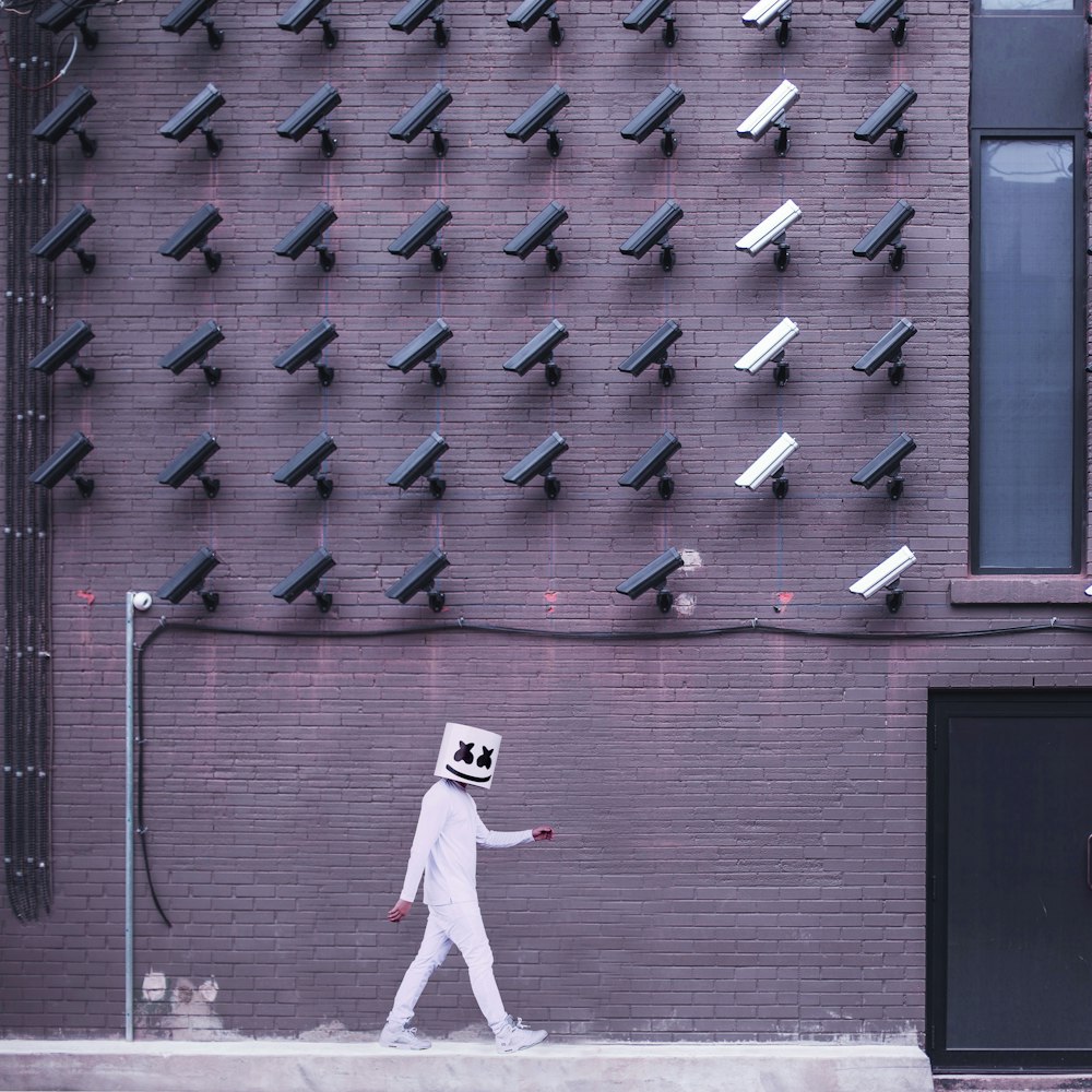 Marshmello walking down the side of the road with camera on the top of the building