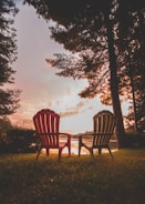 A classic Adirondack chair resting on a wooden deck overlooking a serene lake at sunset.