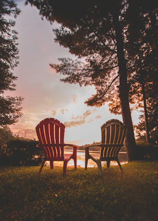 Foldable camping Adirondack chair set up beside a serene lake at sunset.
