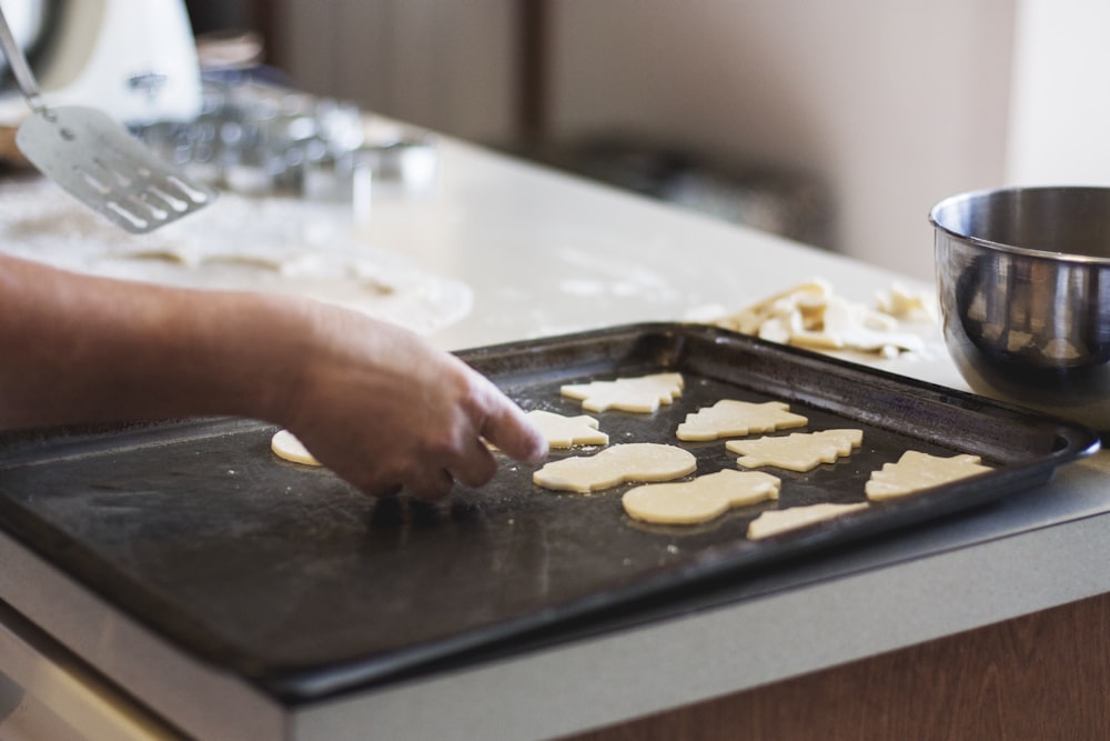 persona forrando galletas de formas variadas en una bandeja para hornear dentro de la cocina