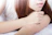 A soft-focus photo of a smiling woman gently touching her smooth forearm in natural light.