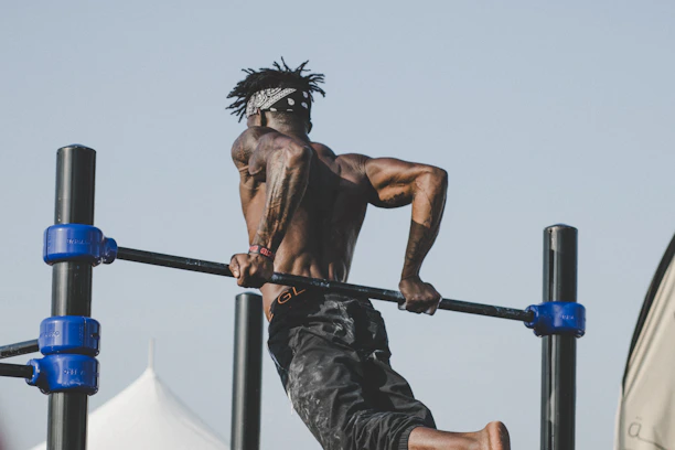 A strong male calisthenics athlete performing a muscle-up on outdoor bars, wearing a fitted compression shirt.