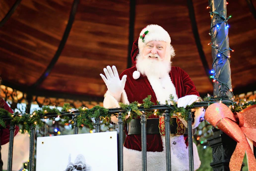 Santa Claus waving warmly in a snowy Central Missouri neighborhood, with twinkling holiday lights in the background.