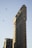 A tall, iconic triangular building with a classic architectural design stands prominently against a clear sky. Two birds are flying in the sky nearby. Part of a lower building with a billboard advertising bourbon is also visible.