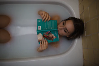 woman lying on bathtub with green book