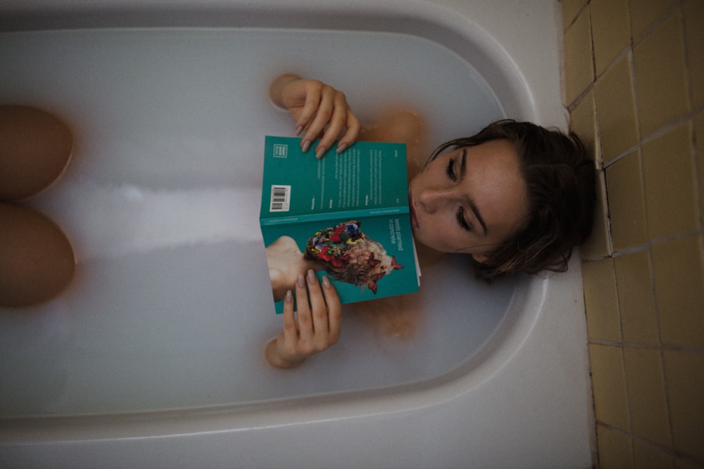 woman lying on bathtub with green book