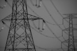 Large metal transmission towers connected by a complex network of power lines. The weather is clear, and the image is in black and white, focusing on the structures' intricate lattice designs.