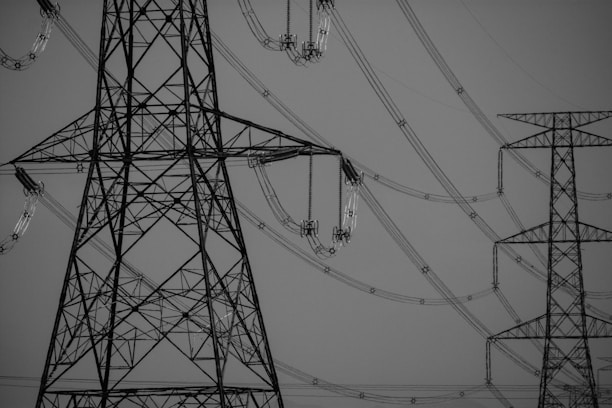 Large metal transmission towers connected by a complex network of power lines. The weather is clear, and the image is in black and white, focusing on the structures' intricate lattice designs.