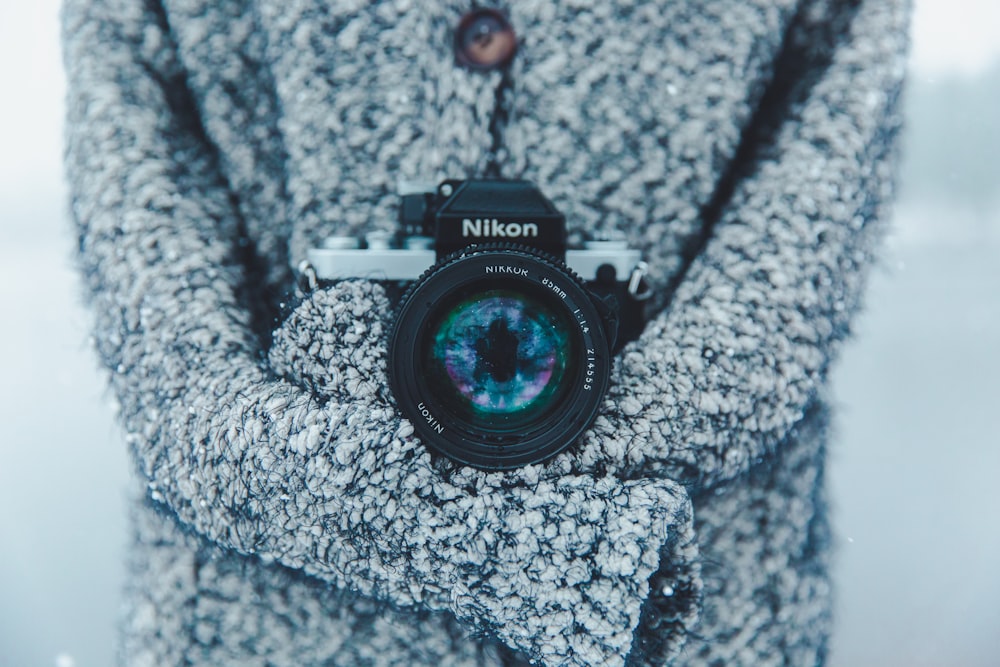 persona che tiene in mano la fotocamera DSLR Nikon nera e grigia