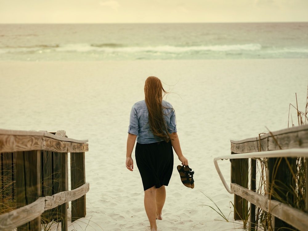 woman holding sandal walking on sand