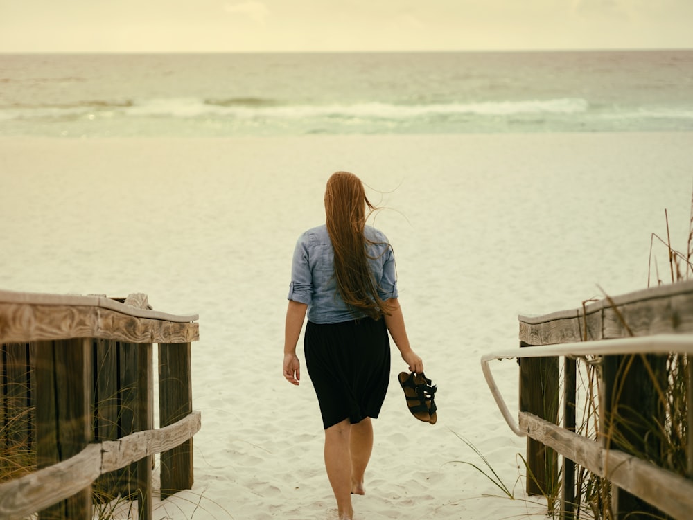 mulher segurando sandália andando na areia