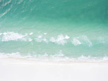Wide shot of a pristine white sand beach with gentle waves and a bright blue sky.