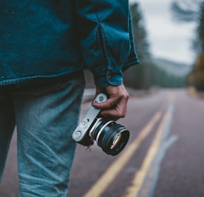 person holding gray and black camera while standing on road