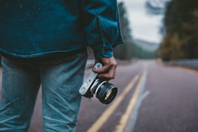 person holding gray and black camera while standing on road