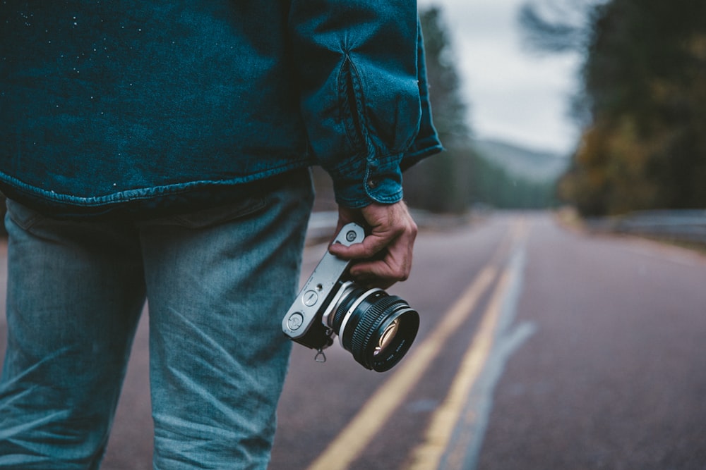 person holding gray and black camera while standing on road