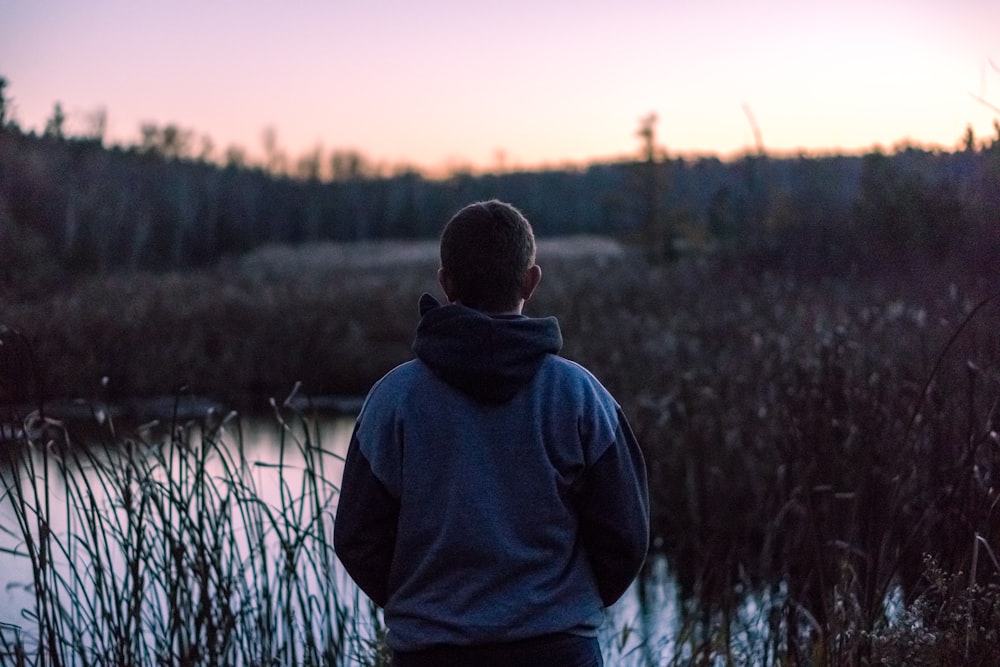 man wearing black and grey hoodie standing near lake