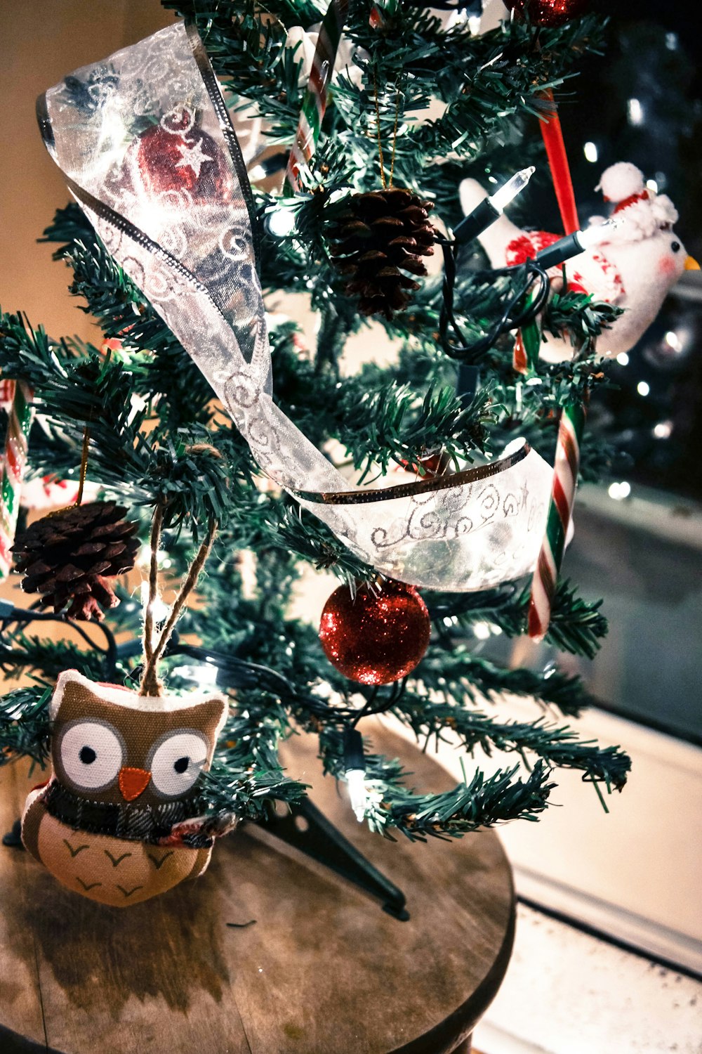 An owl sitting in front of a small Christmas tree.