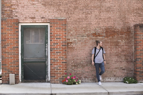 A model wearing a soft gray t-shirt with rolled sleeves, standing outdoors against a brick wall