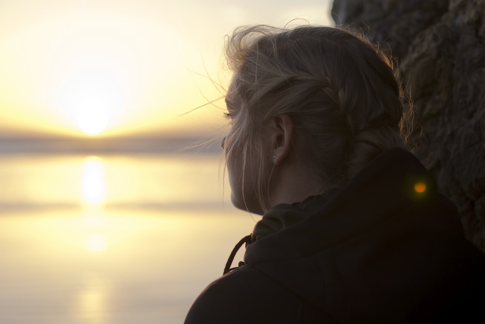 Frau im schwarzen Kapuzenpullover starrt bei Sonnenuntergang auf das Meer