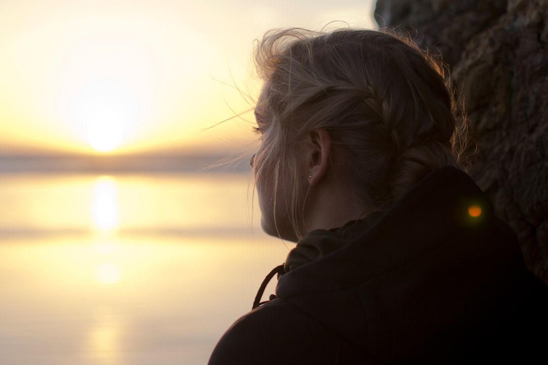 woman in black hoodie staring at the sea at sunset
