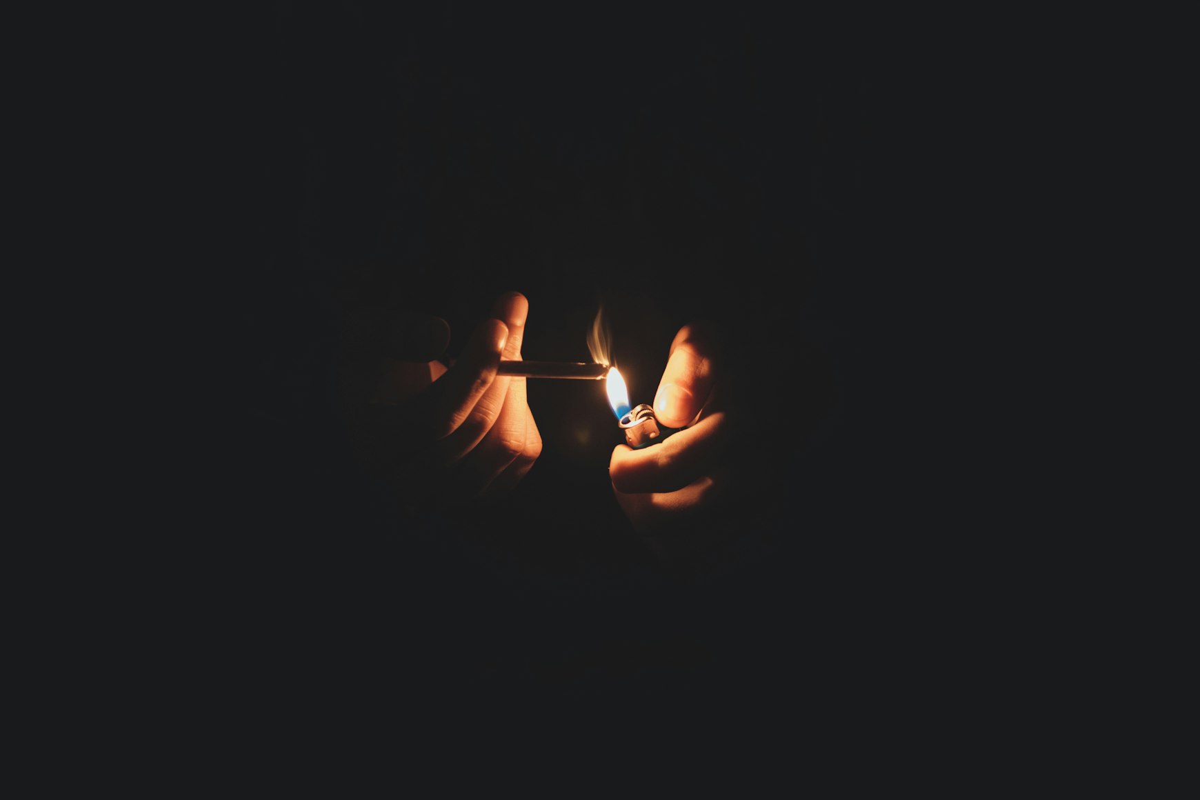 A pair of hands emerge out of the dark to light a blunt