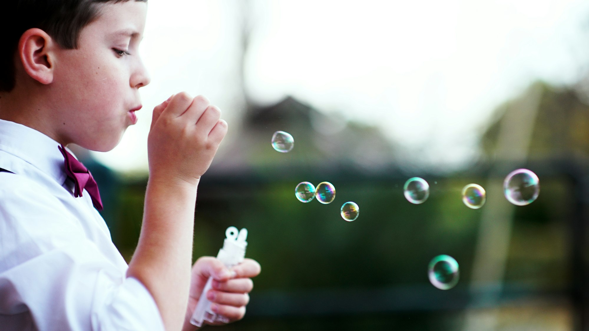 Bambino con camicia bianca e papillon vestito per la prima comunione che gioca con le bolle di sapone 