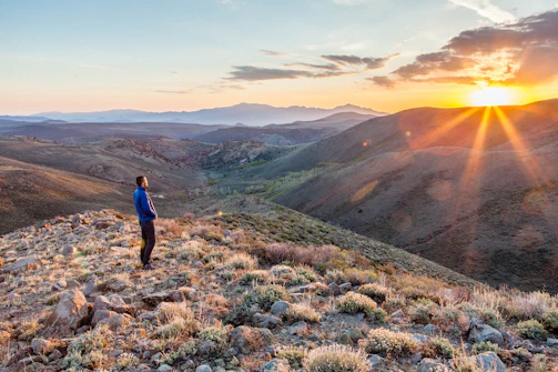 A contemplative man standing at dawn on a rugged cliff, overlooking a vast, awakening landscape.