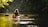 A person is kayaking in a calm river surrounded by dense green foliage. The sunlight filters through the trees, casting a warm glow on the water. The scene is tranquil and serene, with the kayak gliding smoothly across the reflective surface.