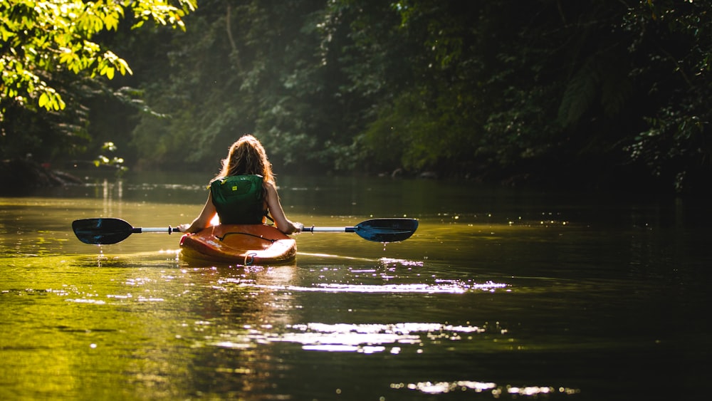 Mujer en kayak en el cuerpo de agua sosteniendo remo