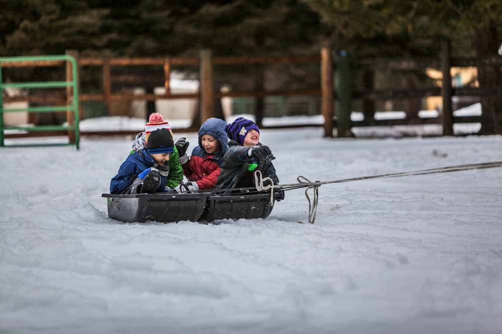 four children riding boat on snow