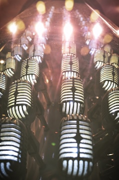 A series of retro-style microphones are arranged in a visually striking pattern, accompanied by reflections that create a vibrant and dynamic effect. The lighting creates a warm, glowing ambiance.