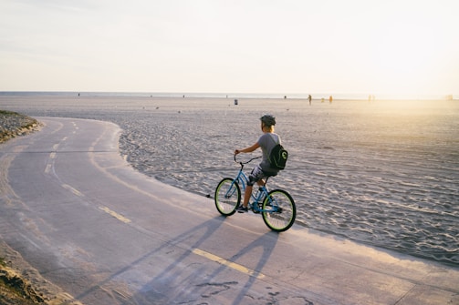 A cyclist riding along a coastal road during sunset.