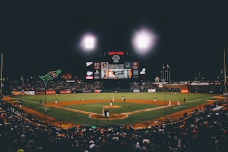 A panoramic shot of a baseball stadium under bright lights during an evening game.