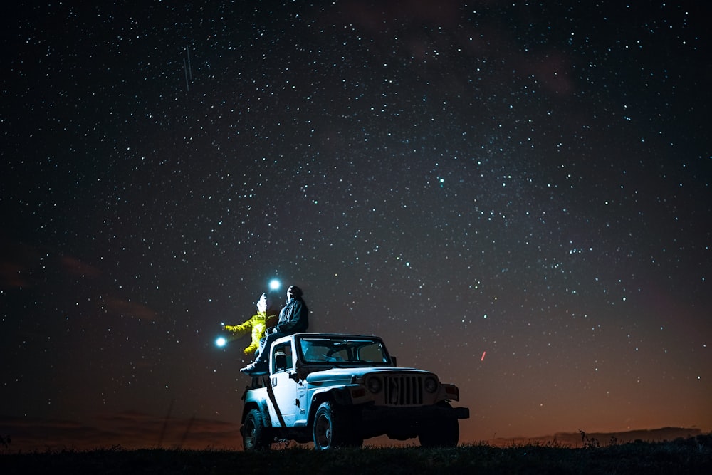 person sitting on top of wrangler under starry sky