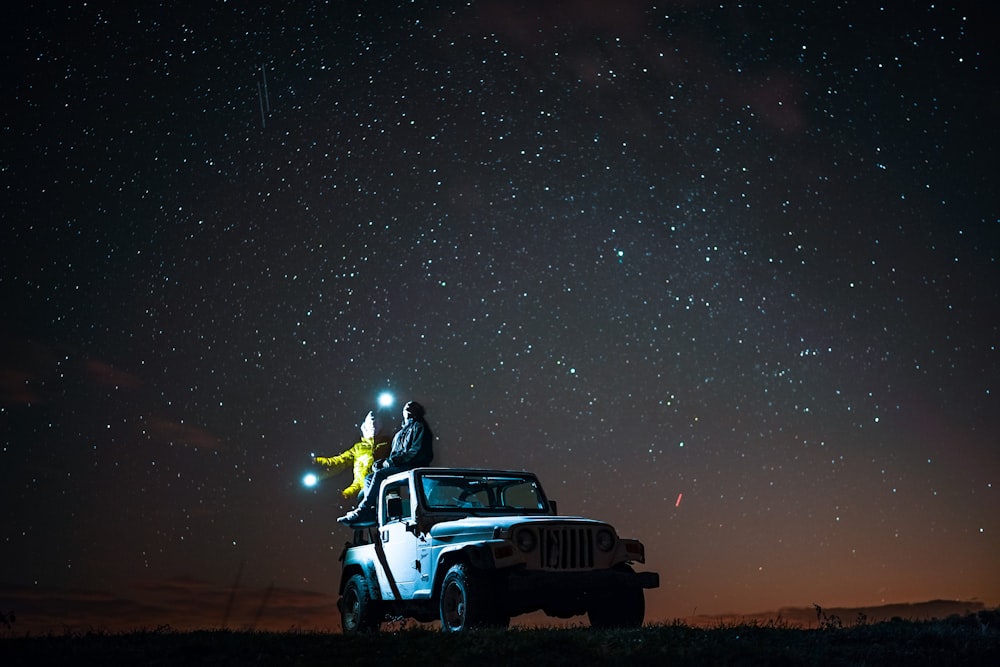 Persona sentada en la parte superior de Wrangler bajo el cielo estrellado