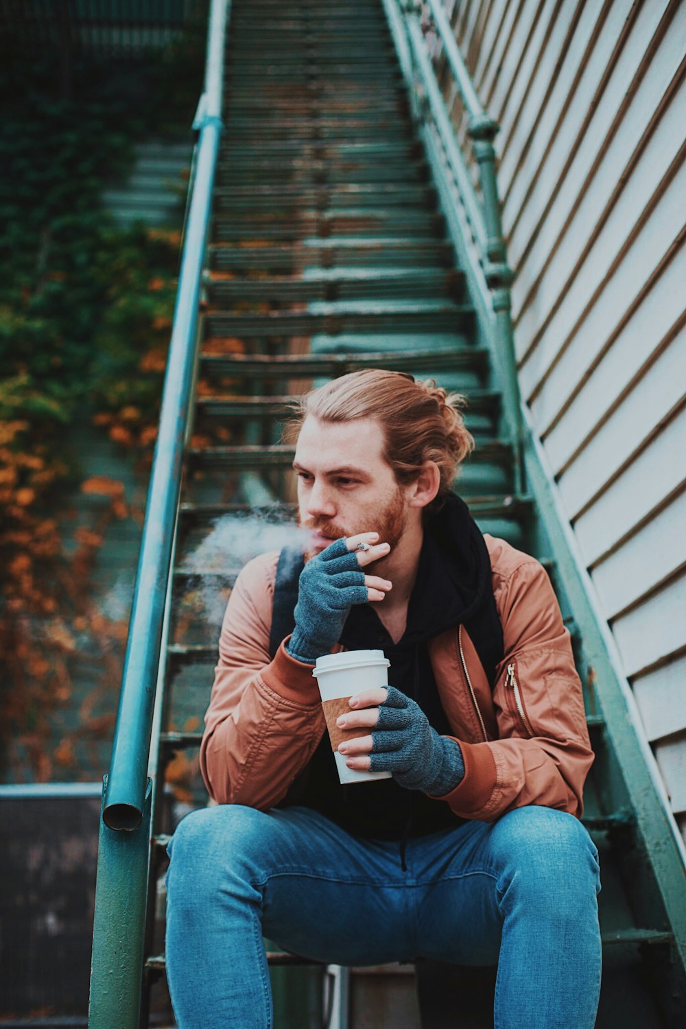 Photographie sélective de mise au point d’un homme fumant assis sur un escalier